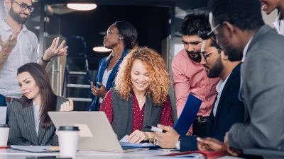 Searching of new insights and brilliant ideas. Mixed-race group of nine diverse people browsing net and looking through documents while sitting at the table in office